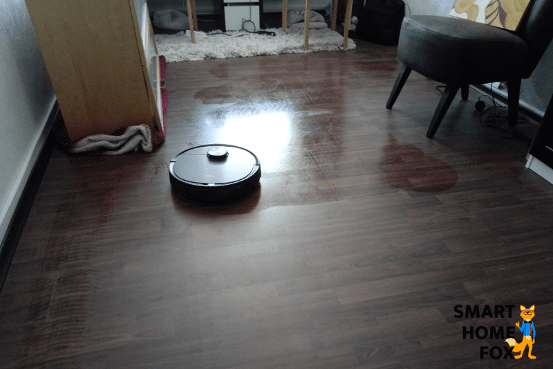 Man sieht, wie ein Saug-Wischroboter den Holzfußboden wischt.